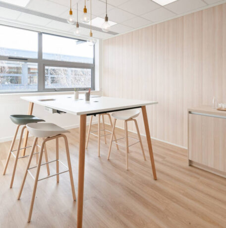 Espace de collaboration en bois avec une table haute et des tabourets multicolores, offrant un cadre dynamique et stimulant pour des sessions de travail en groupe.