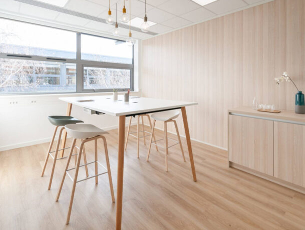 Espace de collaboration en bois avec une table haute et des tabourets multicolores, offrant un cadre dynamique et stimulant pour des sessions de travail en groupe.