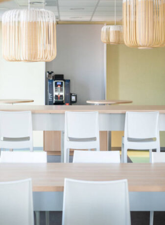 Espace de pause chez OPAC du Rhône, équipé d'installations de cuisine, incluant une machine à café, et des chaises et tables, permettant aux collaborateurs de se détendre et de se restaurer.