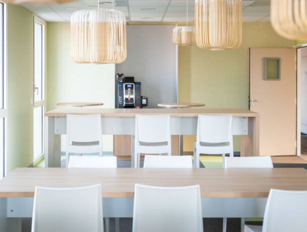 Espace de pause chez OPAC du Rhône, équipé d'installations de cuisine, incluant une machine à café, et des chaises et tables, permettant aux collaborateurs de se détendre et de se restaurer.