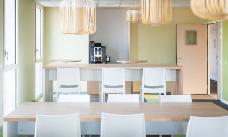 Espace de pause chez OPAC du Rhône, équipé d'installations de cuisine, incluant une machine à café, et des chaises et tables, permettant aux collaborateurs de se détendre et de se restaurer.