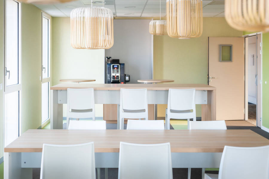 Espace de pause chez OPAC du Rhône, équipé d'installations de cuisine, incluant une machine à café, et des chaises et tables, permettant aux collaborateurs de se détendre et de se restaurer.