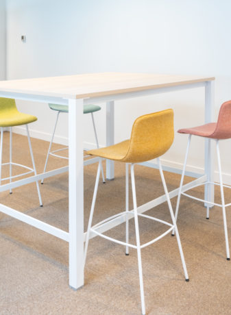 Zone de travail collaboratif chez Dipra, équipée d'une table haute et de tabourets colorés qui permettent une configuration flexible pour les projets d'équipe et les réunions informelles.