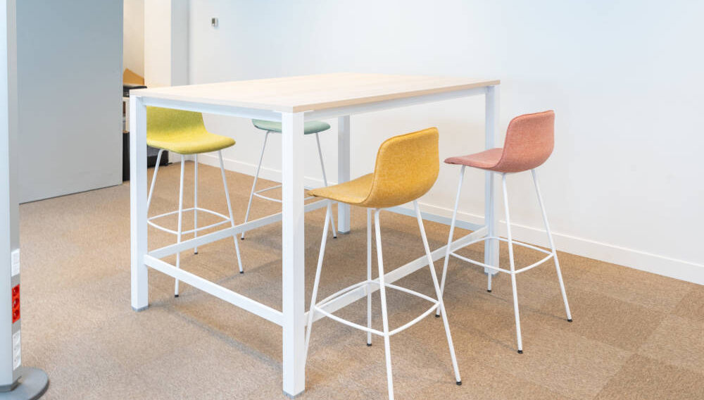 Zone de travail collaboratif chez Dipra, équipée d'une table haute et de tabourets colorés qui permettent une configuration flexible pour les projets d'équipe et les réunions informelles.