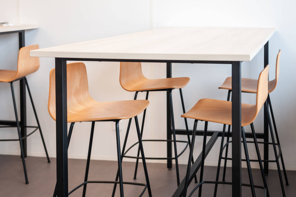 Table haute avec tabourets dans le réfectoire du Leader Mondial de Production de Transducteurs, offrant un espace moderne et pratique pour les repas rapides et les pauses café, tout en favorisant des interactions informelles entre collègues.