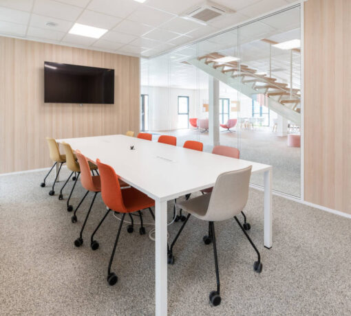 Salle de réunion moderne et bien aménagée avec une grande table U-DESK, des chaises VERSUS confortables et des équipements audiovisuels, illustrant un espace conçu pour faciliter les échanges et la collaboration efficace entre les équipes.