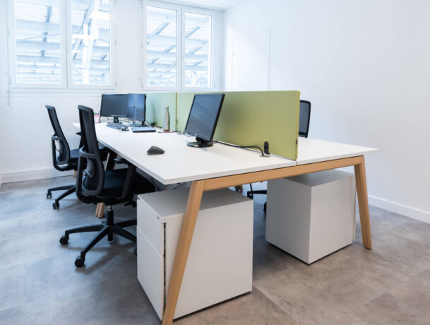 Espace de travail chez Deltalys, illustrant un aménagement moderne scandinave avec des bureaux Woodesk, des cloisons acoustique verte, au couleur de la marque, pour encourager l'interaction.