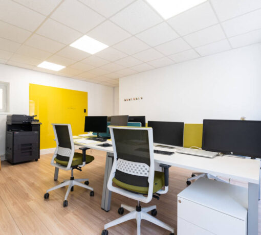 Open space moderne doté de bureaux ergonomiques, de fauteuils adaptés, d'un tableau pour les présentations et de patères murales pour le rangement, assurant un espace de travail pratique et fonctionnel.