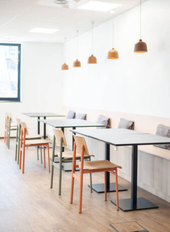 Réfectoire moderne avec des chaises en métal colorées (orange et vert) et des tables Linéa, créant un environnement vibrant et fonctionnel pour les repas et les pauses.