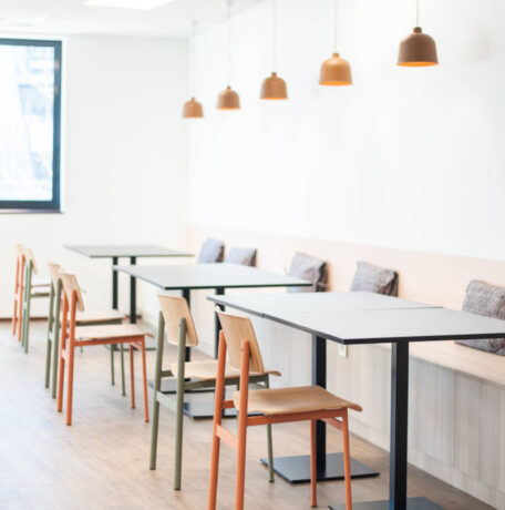 Réfectoire moderne avec des chaises en métal colorées (orange et vert) et des tables Linéa, créant un environnement vibrant et fonctionnel pour les repas et les pauses.