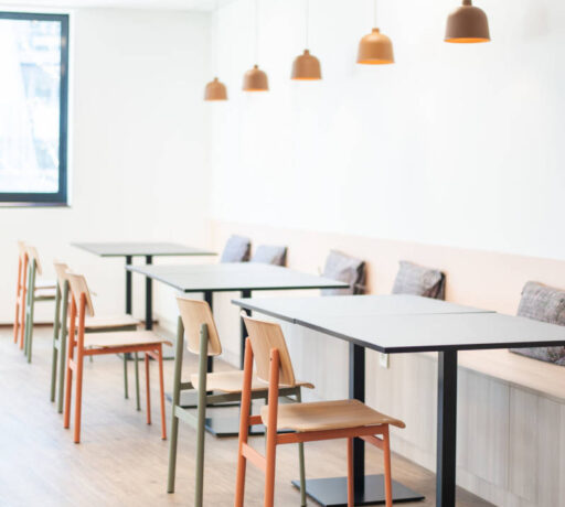 Réfectoire moderne avec des chaises en métal colorées (orange et vert) et des tables Linéa, créant un environnement vibrant et fonctionnel pour les repas et les pauses.