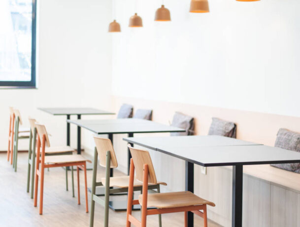 Réfectoire moderne avec des chaises en métal colorées (orange et vert) et des tables Linéa, créant un environnement vibrant et fonctionnel pour les repas et les pauses.