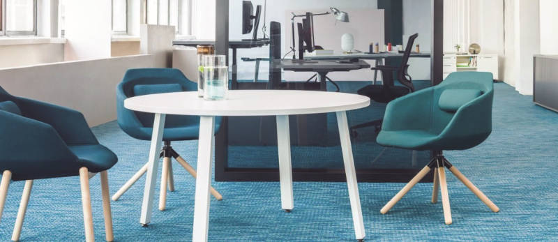 Environnement de bureau avec une table ronde centrale entourée de fauteuils confortables, créant un espace de travail collaboratif et accueillant pour les réunions informelles.